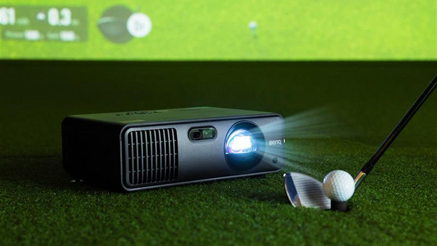 BenQ AK700ST projector on turf in front of a golf simulator screen