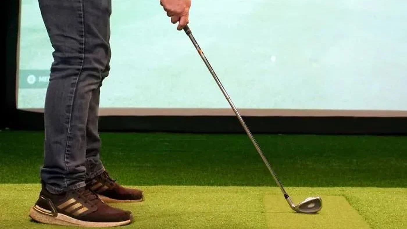 Golfer using a Carl's Place HotShot hitting mat inside an indoor golf simulator for the HotShot 4x5 versus 4x9 comparison.