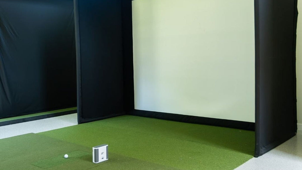 SIG10 golf simulator enclosure with an impact screen and hitting mat in a home room.