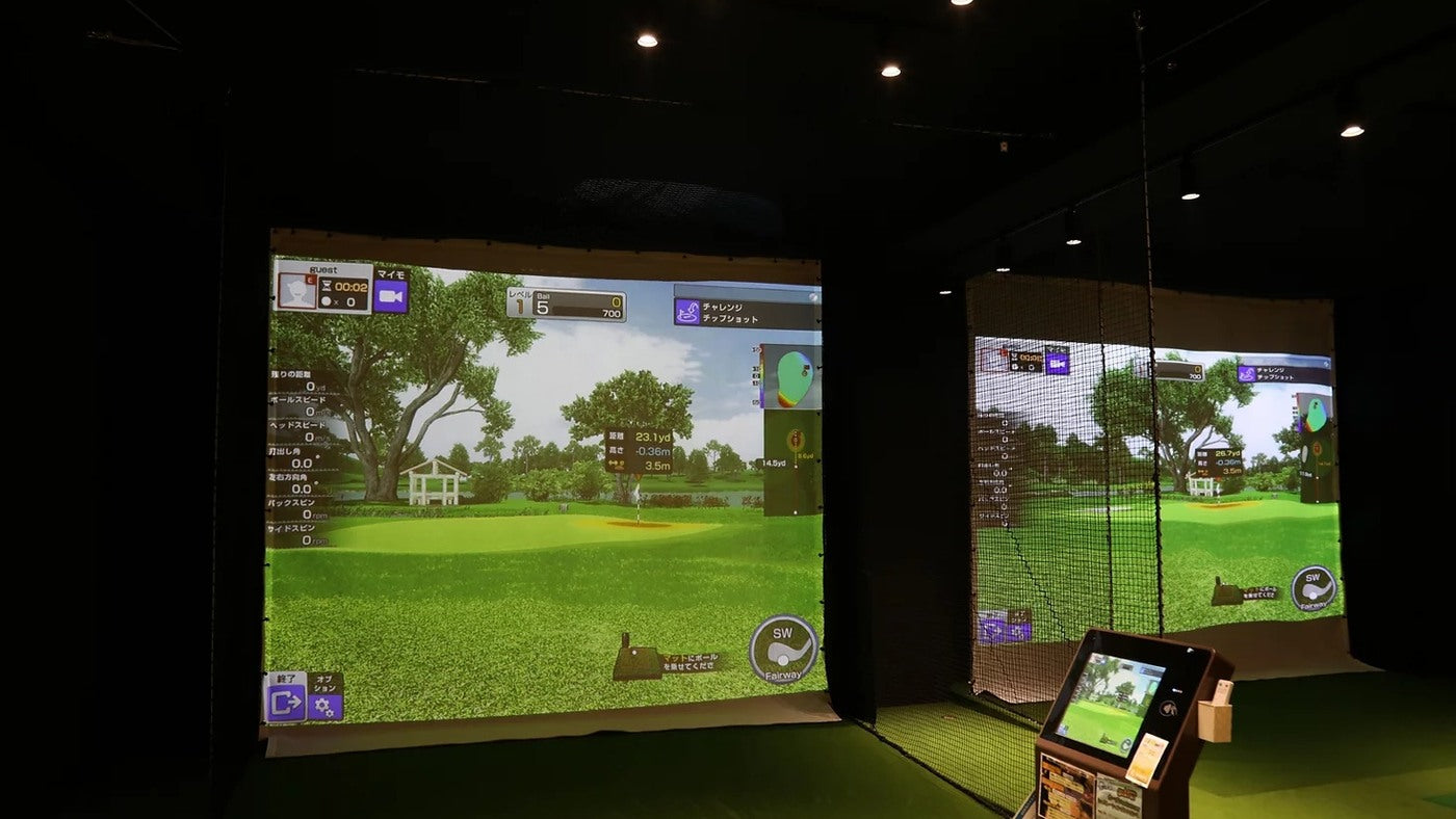 Projected golf courses on impact screens in an indoor room with controlled overhead lighting.