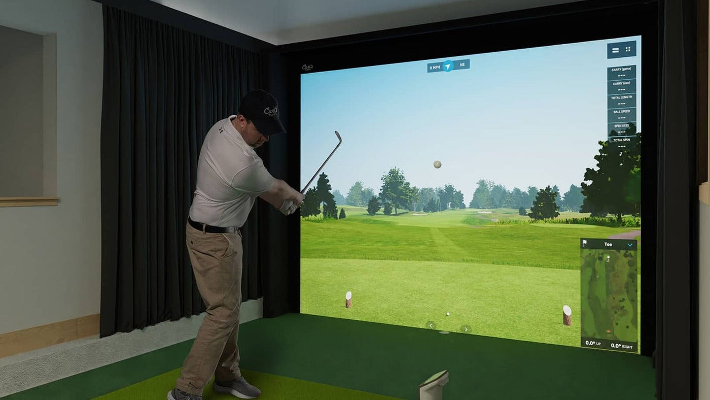 Indoor golf room with a golfer, hitting mat, dark side protection and a projected golf course.