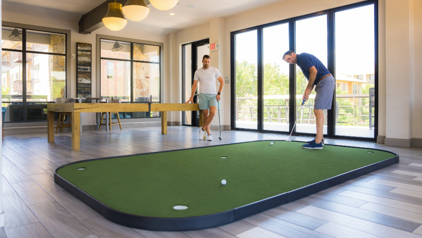 SIGPRO Executive putting green in a bright room with two golfers practicing.