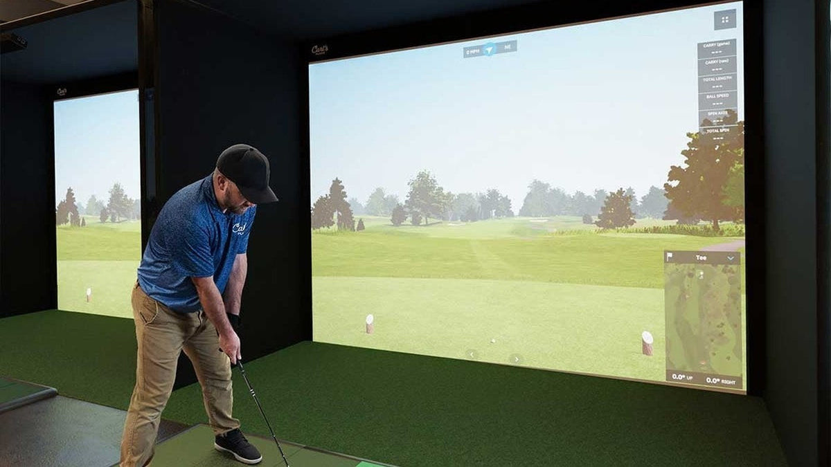 Golfer practicing in an indoor bay with a projected course